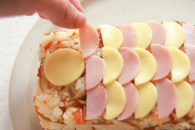 ハムとチーズを交互に並べてうろこを作ろう。丸のままのチーズは目玉になる|コンビニで買える食材で作れる!こどもの日のメニューにおすすめのレシピ!簡単&かわいい鯉のぼりの押し寿司でお祝いしよう