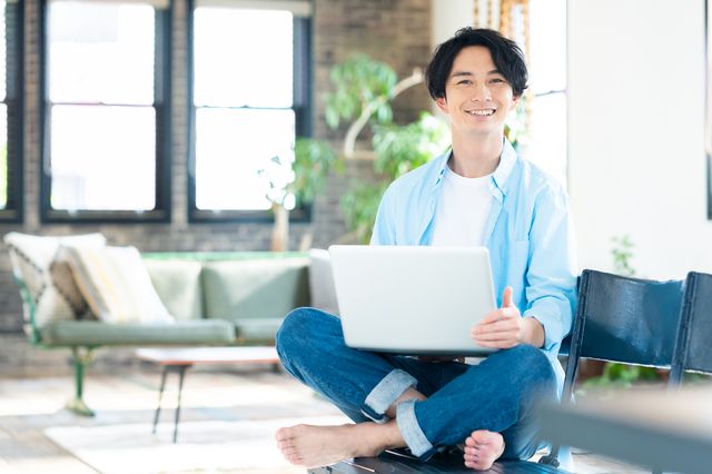 パソコンも持ちながらながら微笑む男性