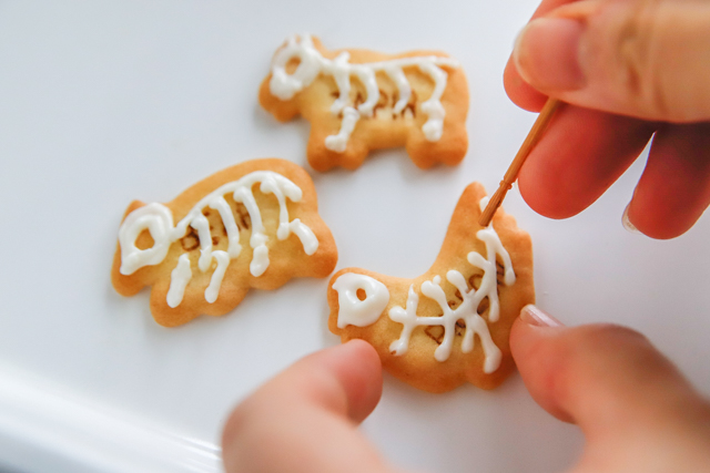 【超簡単ハロウィンスイーツ】ビスケットにチョコペンで骨を描き、つまようじで整える様子
