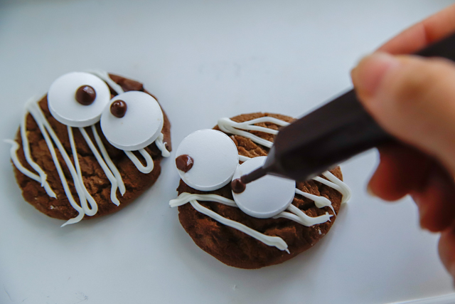 【超簡単ハロウィンスイーツ】クッキーにラムネを載せ、チョコペンで目を描く様子