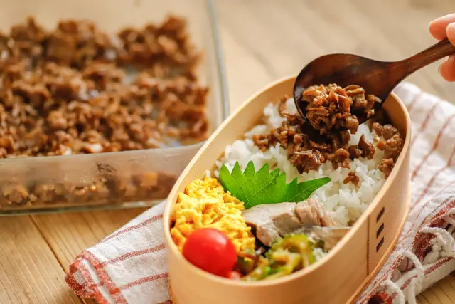 一人暮らし作り置きレシピ「肉ときのこの甘辛そぼろ」をお弁当のご飯にかけている様子