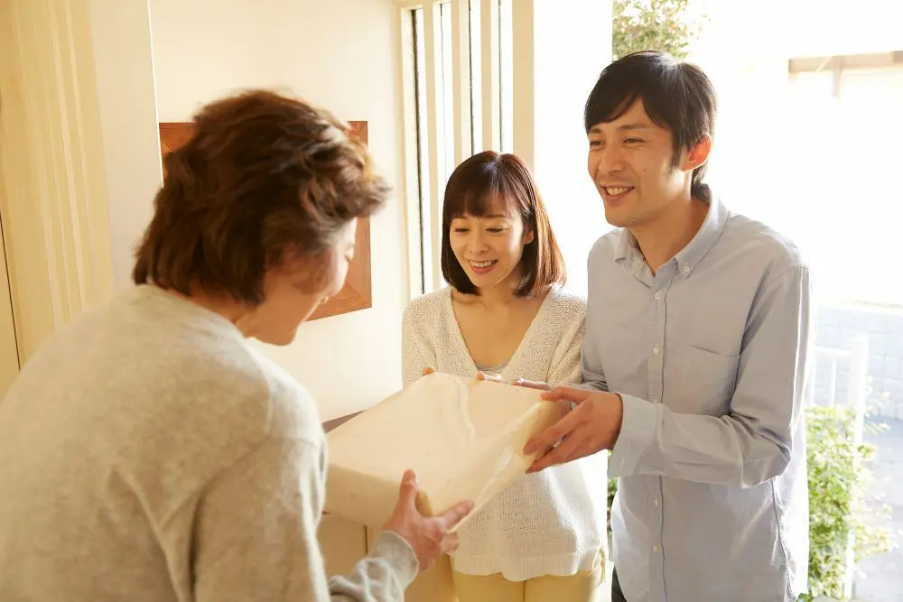 玄関先で菓子折りを渡して挨拶をするカップル