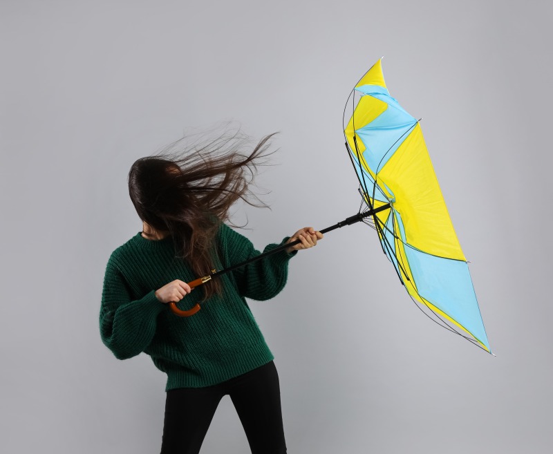 強風で傘を引き飛ばされそうになっている女性