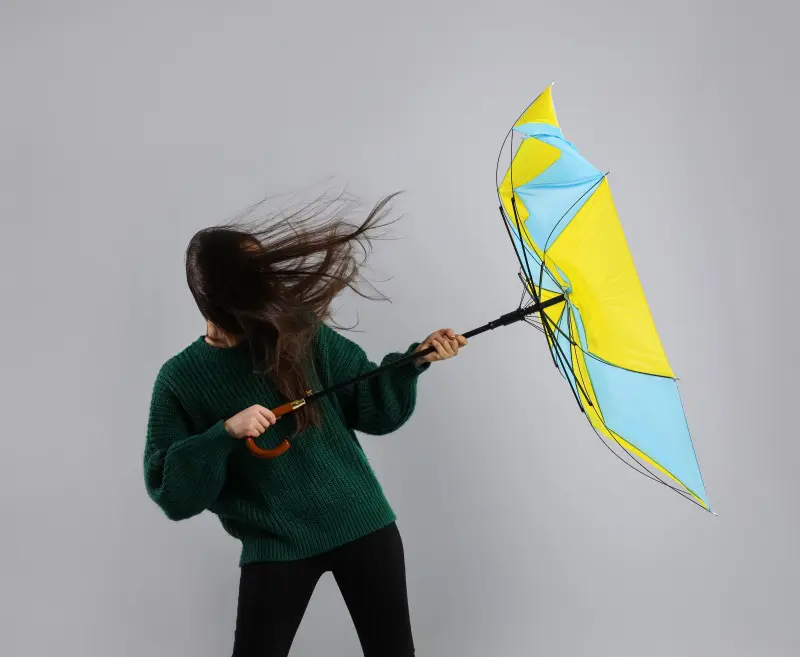 強風で傘を引き飛ばされそうになっている女性