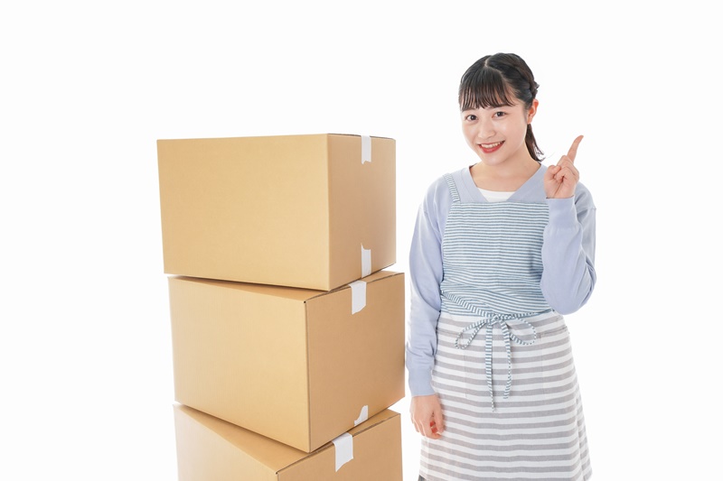 引越しダンボールの横でほほ笑む女性