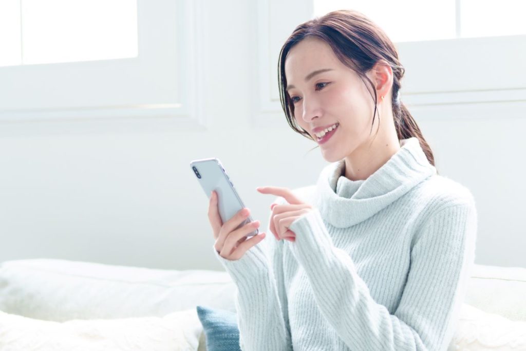 ソファに座り、スマホで部屋探しをする女性