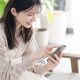 室内でソファに座り笑顔でスマートフォンを操作する女性の写真